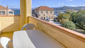 Un balcón con mesa y sillas, con vistas a la costa, edificios y montañas.
