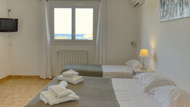 Habitación de hotel con dos camas, televisión, ventana con cortinas, radiador y lámpara.