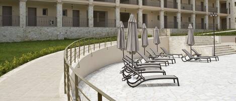 A multi-story hotel with outdoor seating areas, a stone facade, and a mountainous backdrop.