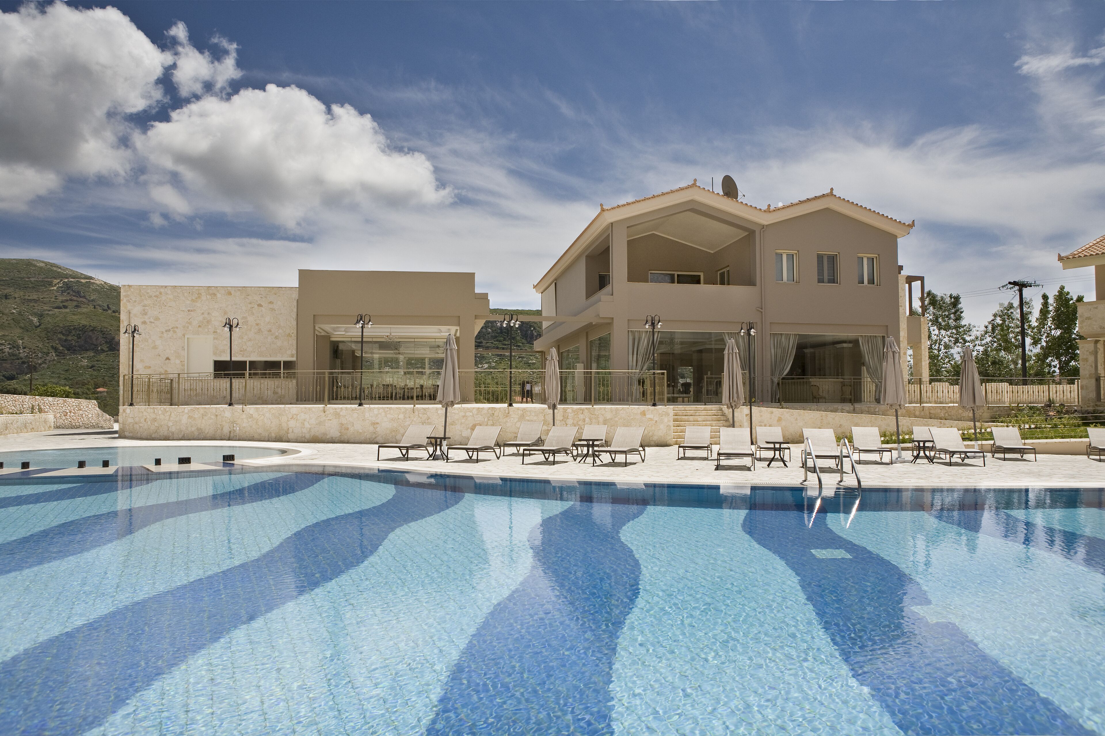 A swimming pool with lounge chairs and a building with large windows and a balcony.