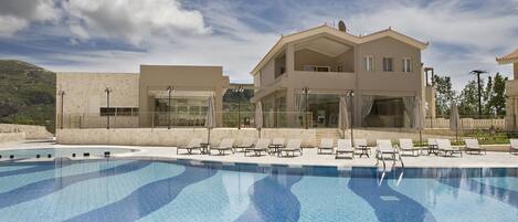 A swimming pool with lounge chairs and a building with large windows and a balcony.