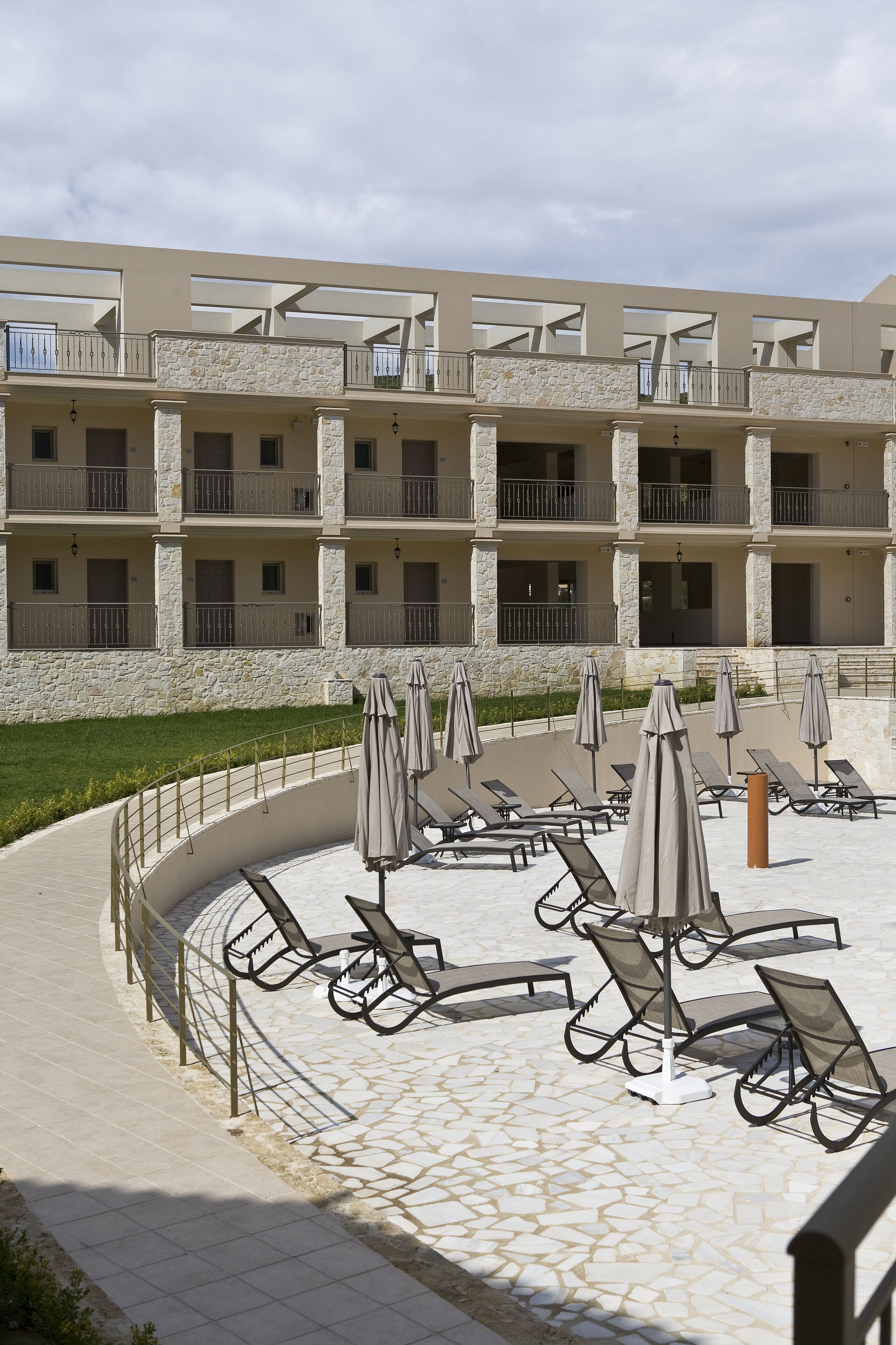 A hotel with a stone facade, multiple balconies, and outdoor seating with umbrellas.