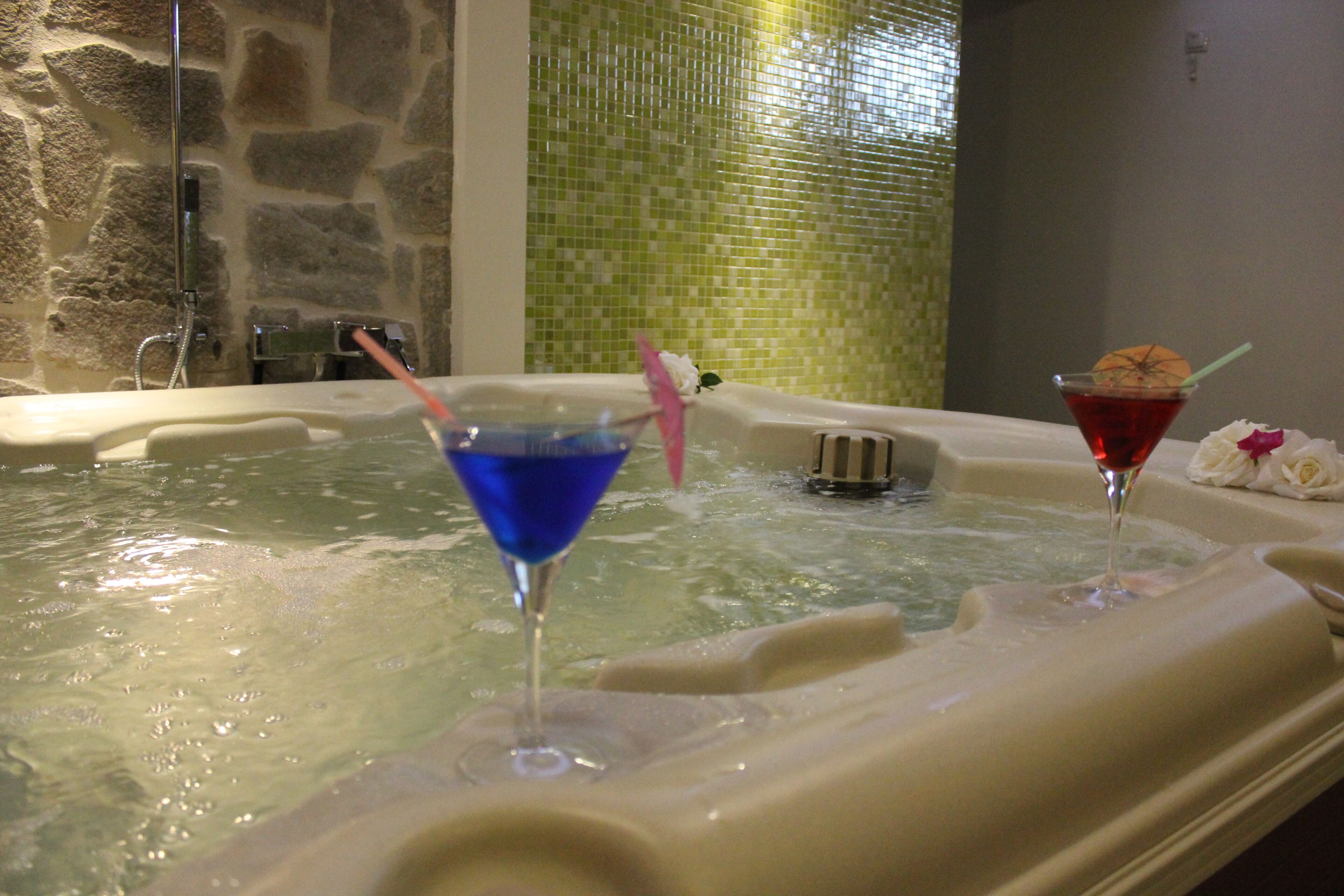 A hot tub with two drinks, one blue and one red, and a flower.