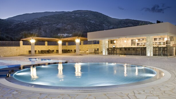 A pool area with a bar and outdoor seating, surrounded by stone tiles and a mountain backdrop. - The Magnolia Resort - Adults Only (Kefalonia)