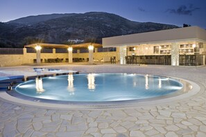 A pool area with a bar and outdoor seating, surrounded by stone tiles and a mountain backdrop. - The Magnolia Resort - Adults Only (Kefalonia)