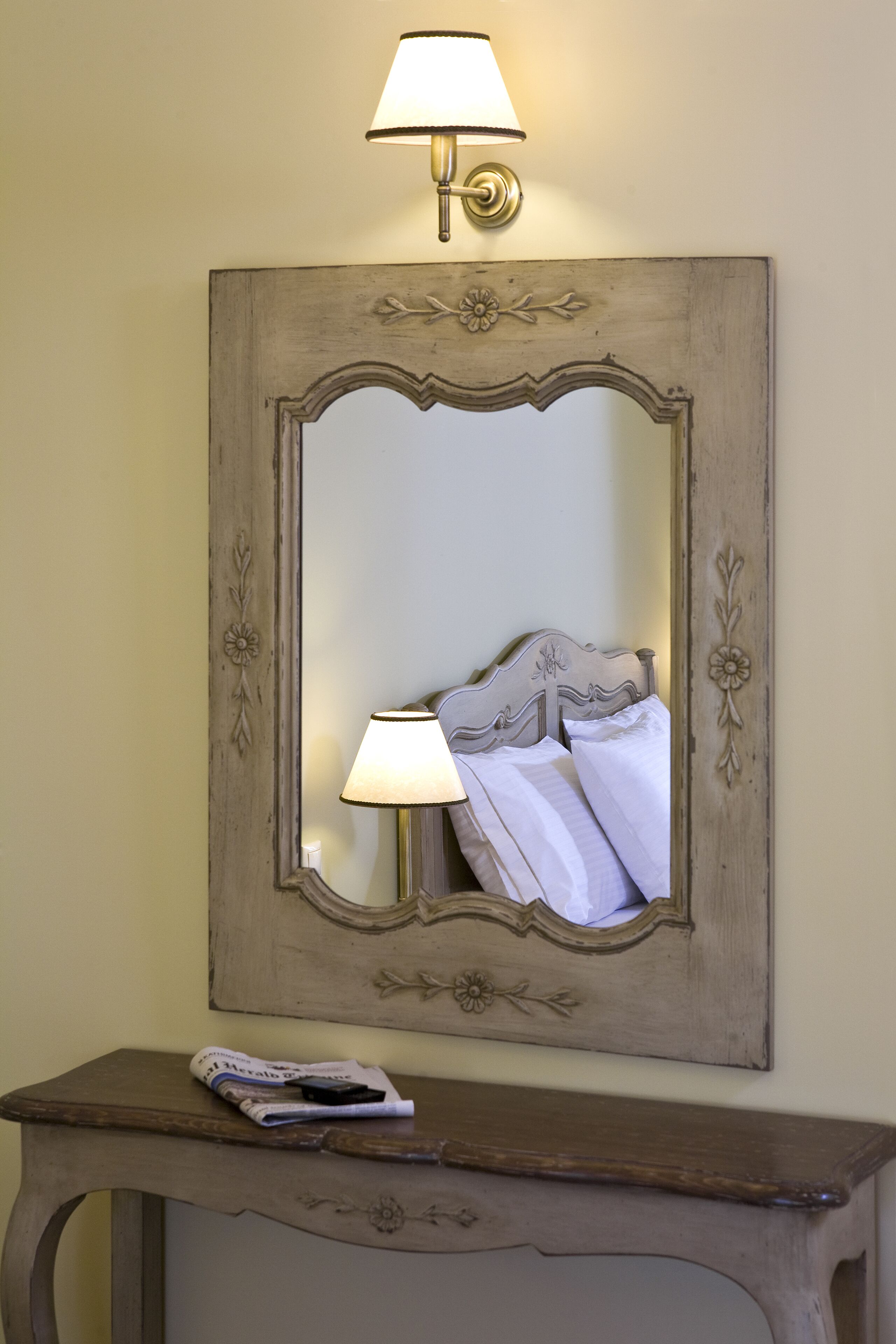 A mirror with a decorative frame, a bedside lamp, and a small table with a magazine.