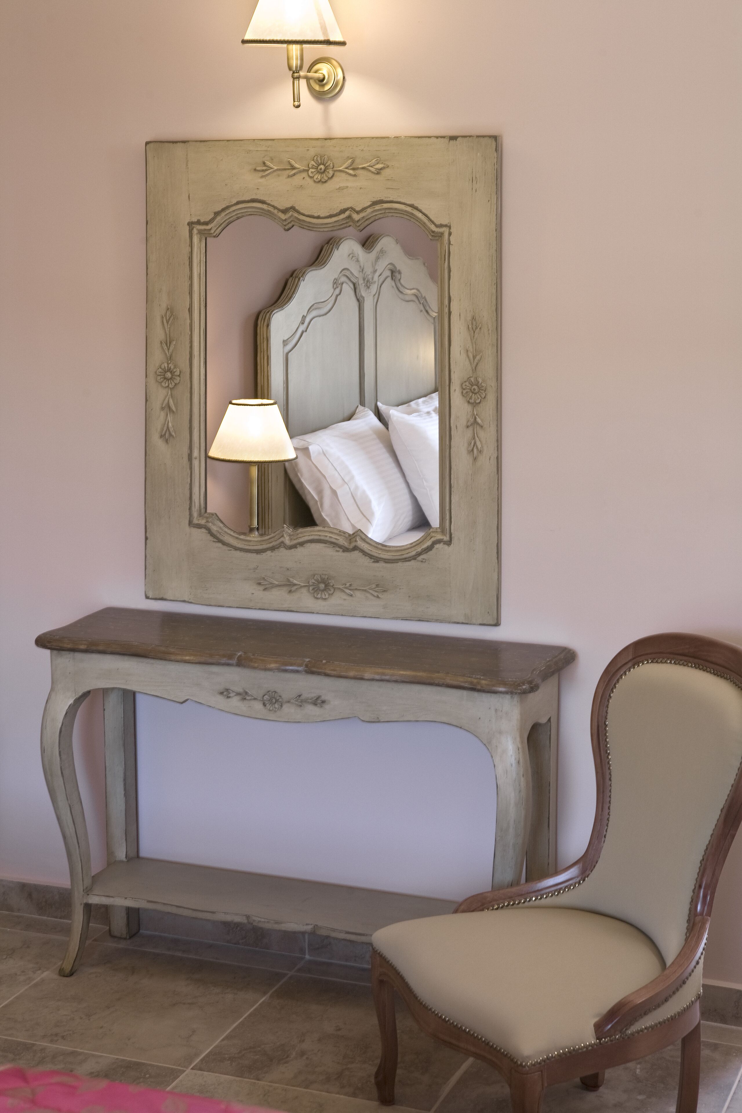 Una consola de estilo vintage con un espejo encima, una silla al lado y una lámpara fijada a la pared.