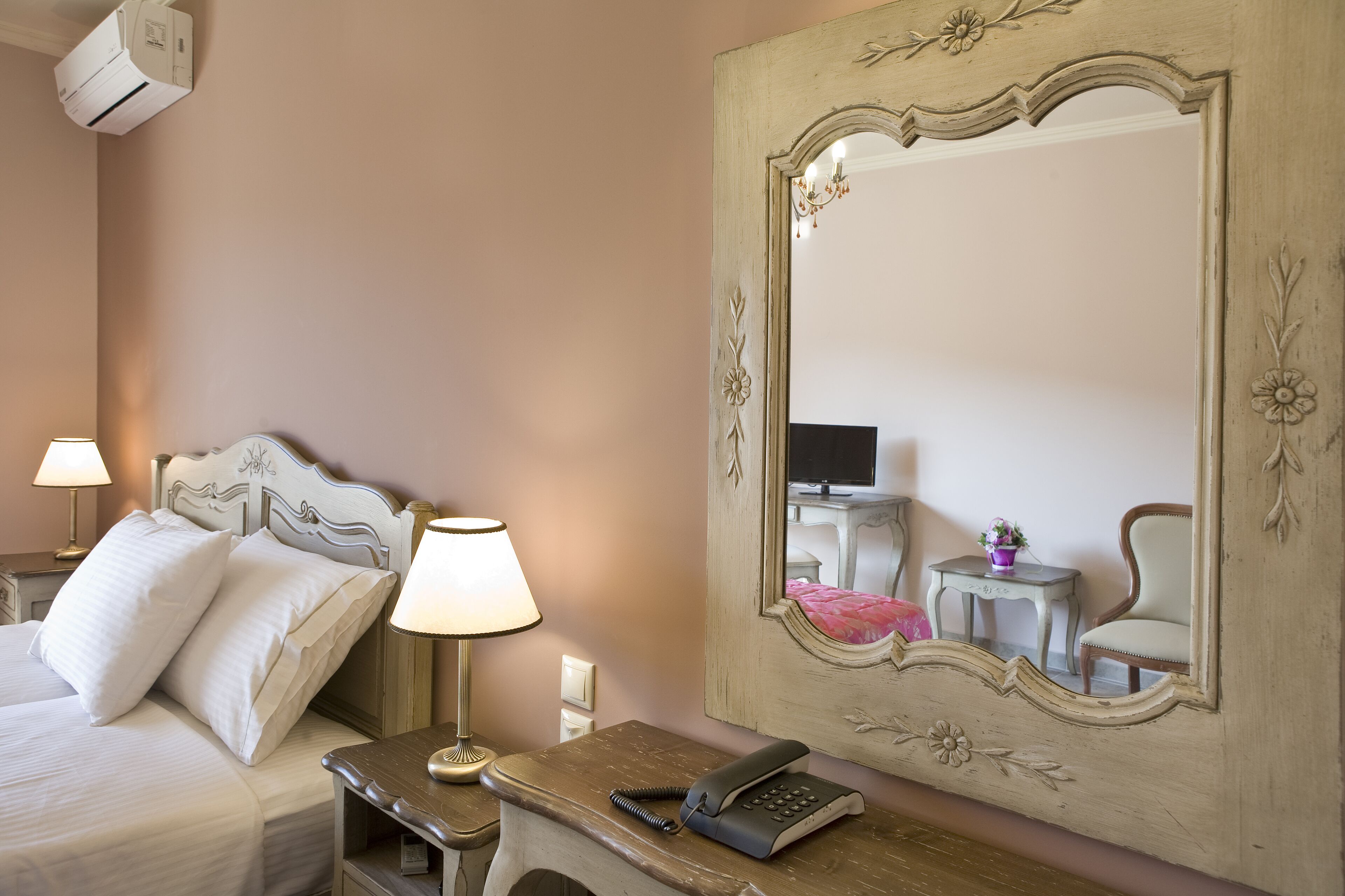 A hotel room with a bed, bedside lamps, a telephone, a mirror, and a small table with a flower vase.