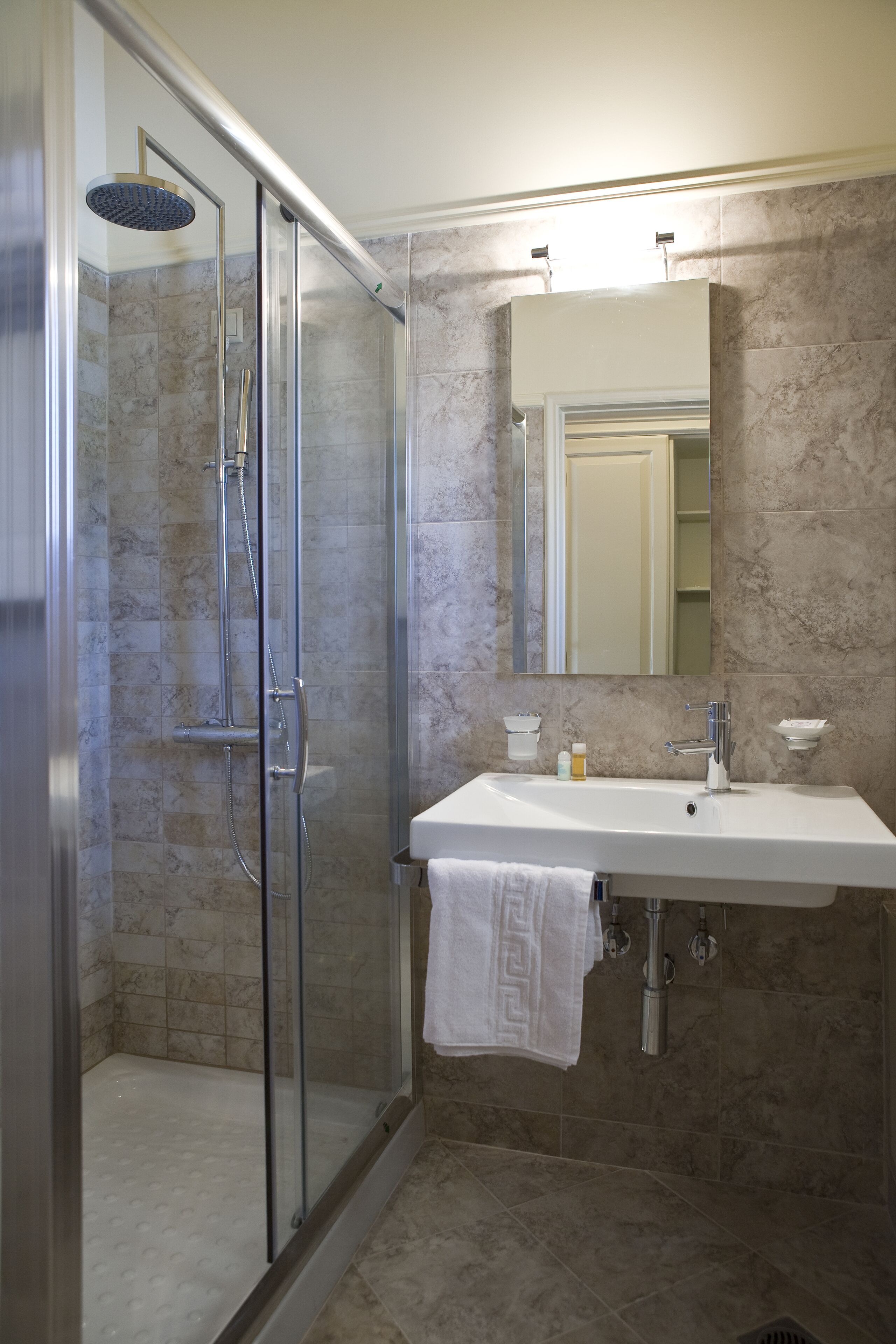 A bathroom with a glass-enclosed shower, a white sink, and a mirror above it.