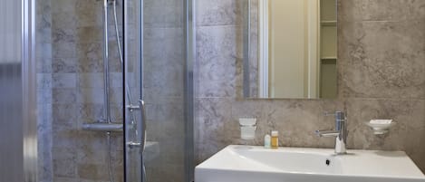 A bathroom with a glass-enclosed shower, a white sink, and a mirror above it.