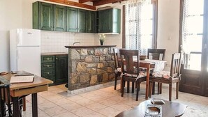 A kitchen with green cabinets, a stone island, and a dining area with chairs. - Traditional Charming Stone Chalet (Distomo-Arachova-Antikyra)