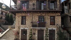 A two-story stone building with a balcony, a staircase leading to the entrance, and potted plants. - Antique Luxury Groundfloor Suite (Kalavrita)