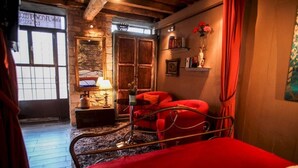 A cozy room with a bed, a red sofa, a wooden door, and a stone wall. - Antique Luxury Groundfloor Suite (Kalavrita)