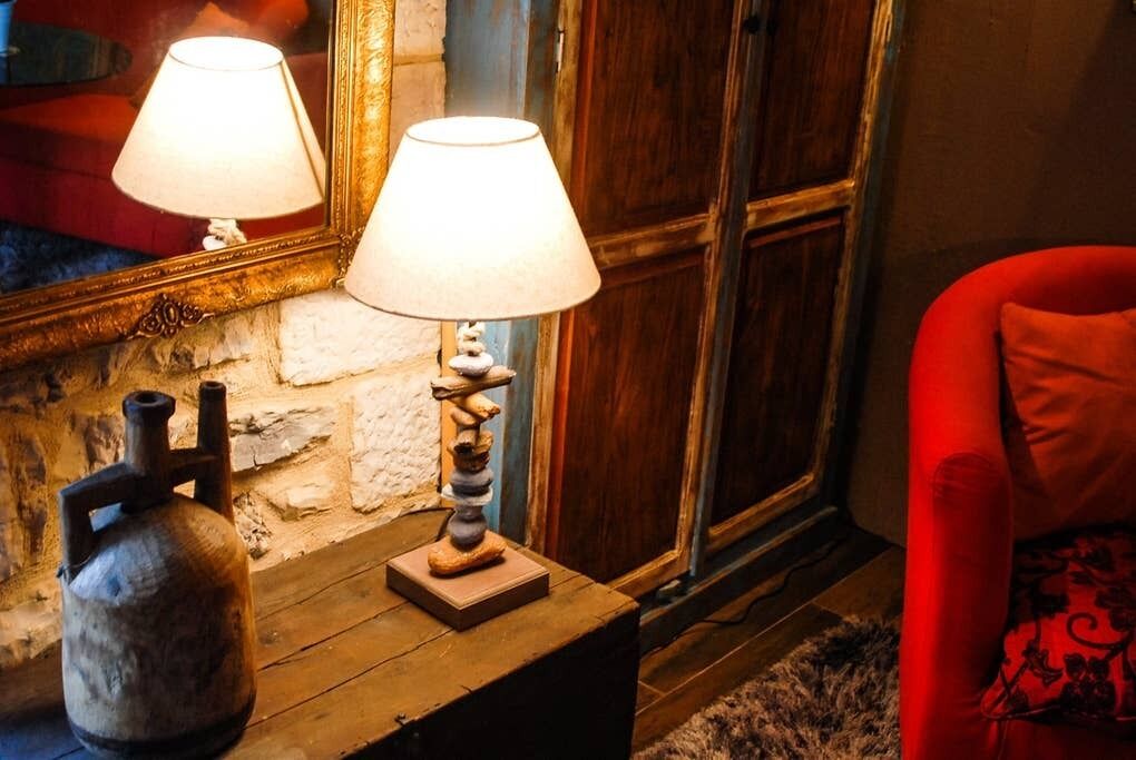 Una stanza con un tavolo di legno, un fornello a gas, una sedia rossa e uno specchio con una lampada.