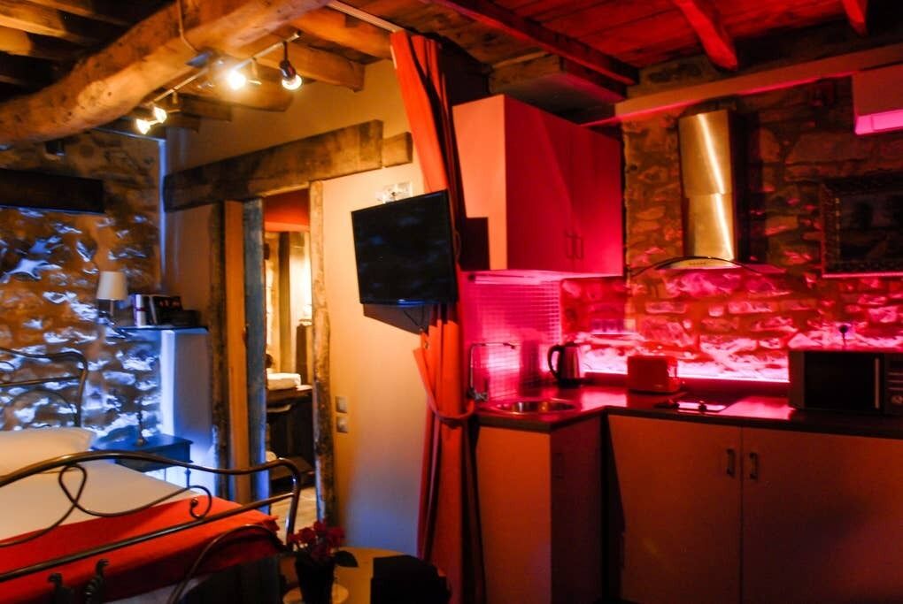 A cozy room with a bed, a television, a kitchen area with a microwave, and a stone wall.