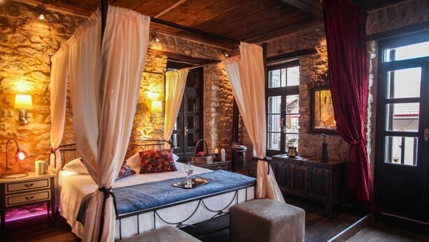 Un dormitorio rústico con pared de piedra, cama con dosel y techo de madera.