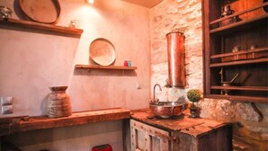 Una cocina rústica con paredes de piedra, estantes de madera y una olla de cobre.