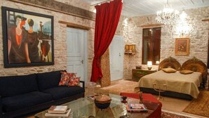 A room with a stone wall, a bed with a wooden headboard, a red curtain, a chandelier, and a painting on the wall. - Antique Luxury Suite 75sq.m. (Kalavrita)