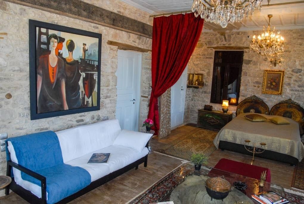Quarto com parede de pedra, sofá branco, cama com cortina vermelha e um candelabro.