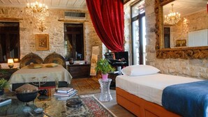A room with a stone wall, a bed with a blue blanket, a wooden headboard, a red curtain, a mirror, and a chandelier. - Antique Luxury Suite 75sq.m. (Kalavrita)
