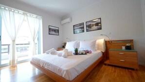 A bedroom with a wooden bed, white bedding, a nightstand, a dresser, and a window with sheer curtains. - New Superb & Luminous 2 Bedroom Apartment (Kifisia)