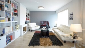A modern living room with a white sofa, a glass coffee table, a bookshelf, and a black and brown rug. - New Superb & Luminous 2 Bedroom Apartment (Kifisia)