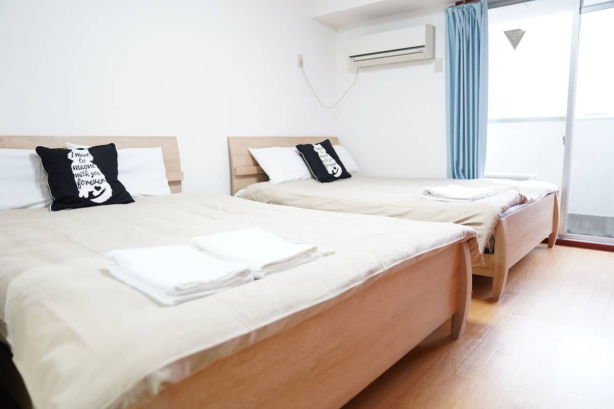 Habitación de hotel con dos camas, cada una con almohada blanca y negra, y una toalla blanca doblada con cuidado sobre la cama.