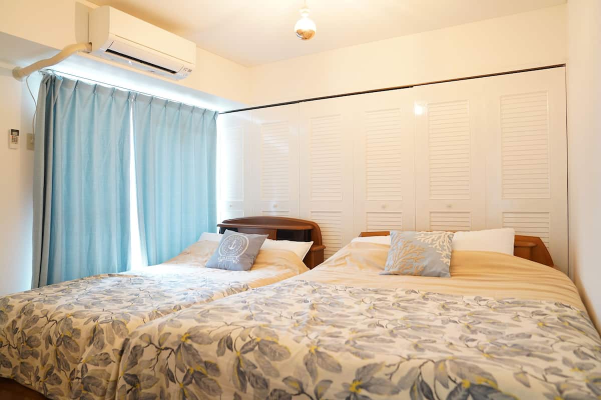 Un dormitorio con dos camas, un ventilador de techo y una ventana con cortinas.