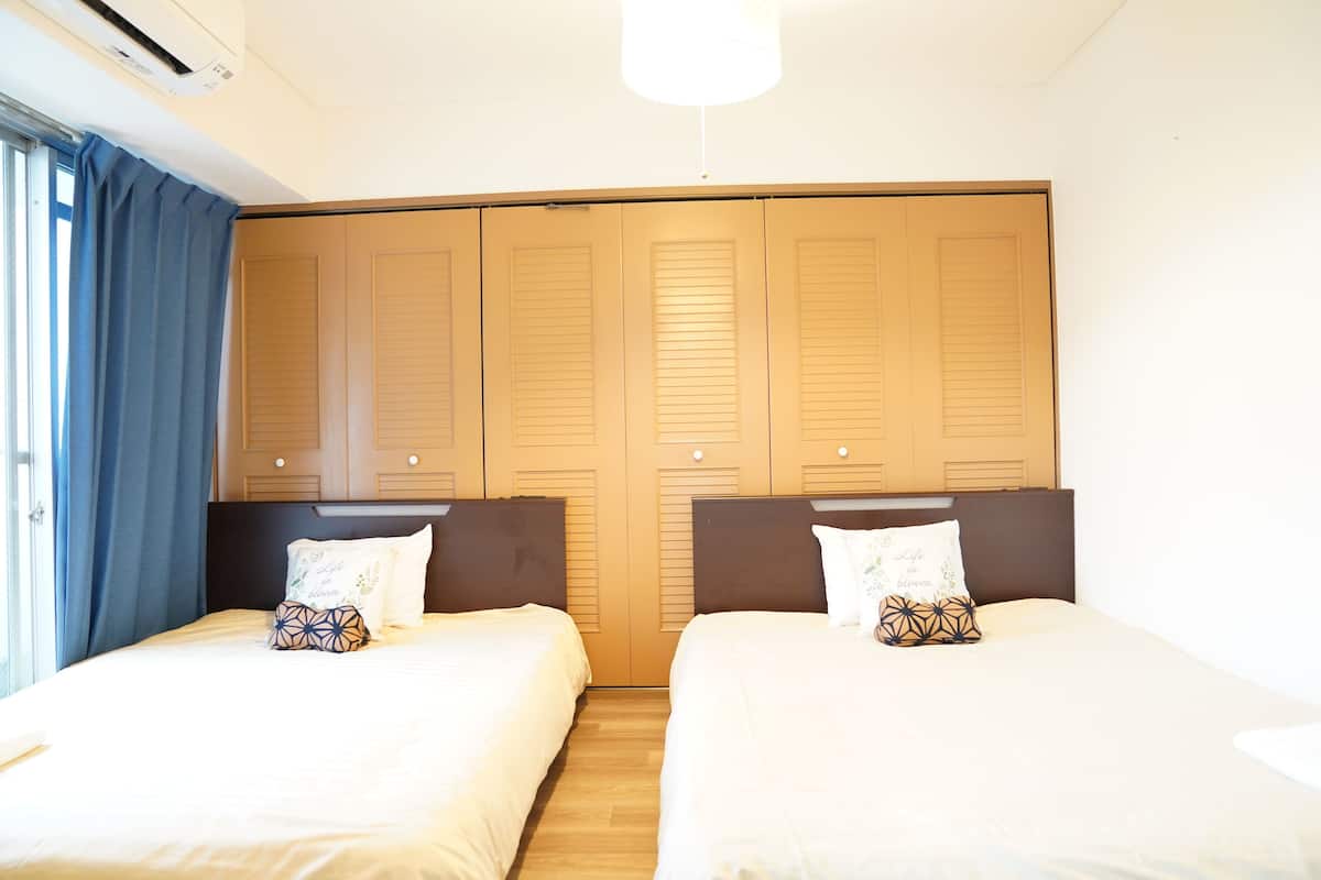 Una habitación de hotel con dos camas, un armario grande y un ventanal con cortinas.