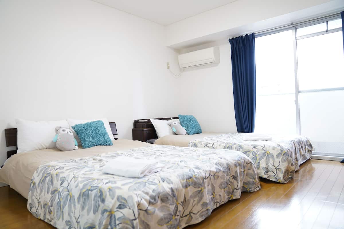 Habitación de hotel con dos camas, un ventanal con cortinas y un equipo de aire acondicionado en la pared.