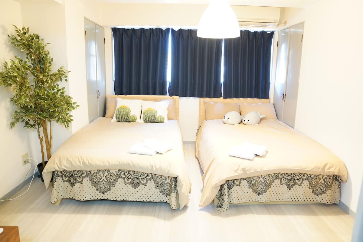 Una habitación con dos camas, una planta en maceta y un ventanal con cortinas.