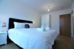 A neatly made bed with white linens, a black headboard, and a bedside table with a lamp.
