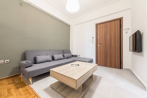 A modern living room with a grey sofa, a wooden coffee table, and a wooden door. - Vibrant Cozy Flat Near the Metro (Alimos)
