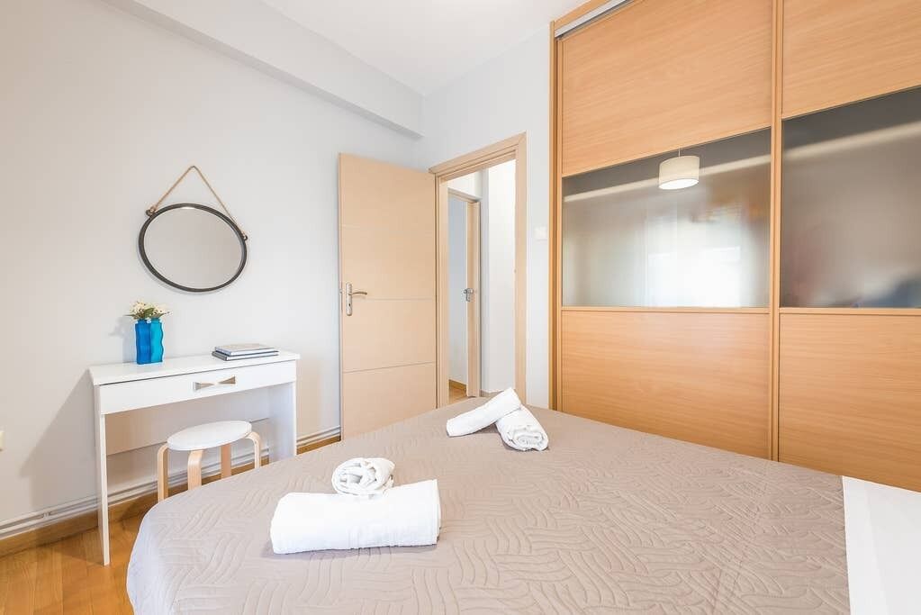 A hotel room with a bed, a desk, a chair, a wardrobe, and a mirror on the wall.