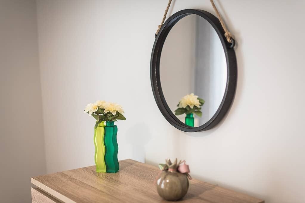 Une commode en bois, ornée de deux vases contenant des fleurs et d’un miroir doté d’une anse en corde.