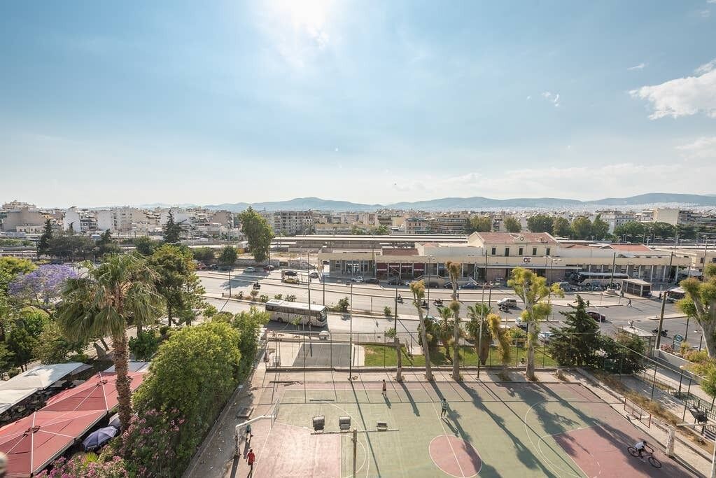 An outdoor basketball court surrounded by buildings, trees, and a clear sky.