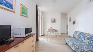 Una sala de estar con sofá, televisión, microondas y una mesa de comedor con sillas.