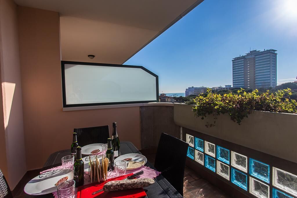 Varanda com mesa posta para dois, garrafa de vinho e vista para a cidade.