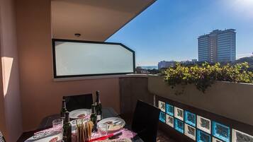 Varanda com mesa posta para dois, garrafa de vinho e vista para a cidade.