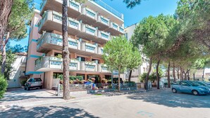 Un hotel de varios pisos con balcones, una zona de estacionamiento y árboles circundantes.