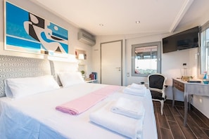 A hotel room with a large bed, a desk, a chair, a TV, and a window with a city view.