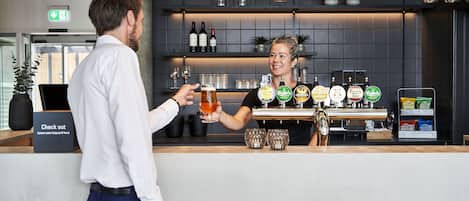 Zona de bar con un cantinero, una selección de grifos de cerveza y varios vasos exhibidos en estantes.