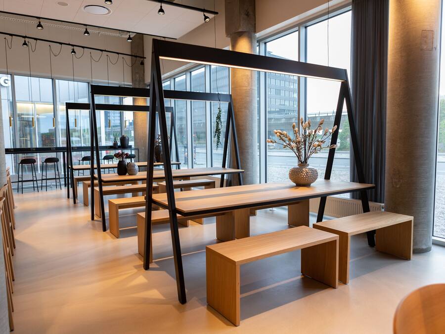 Un intérieur moderne avec des tables et des bancs en bois, de grandes fenêtres offrant une vue sur la ville et un design minimaliste.