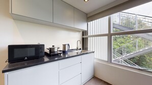 Una cocina moderna con microondas, hervidor y estufa, una ventana con vista a un balcón, y armarios blancos.