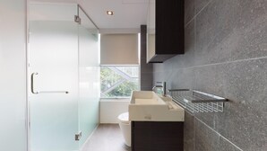 Un baño moderno con mampara de vidrio, un lavamanos blanco y una pared revestida de baldosas oscuras.