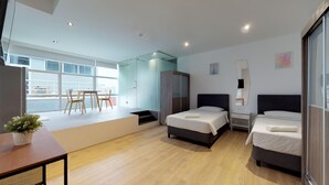 Una habitación de hotel moderna con dos camas, un comedor con mesa y sillas, y un ventanal que ofrece vistas al exterior.