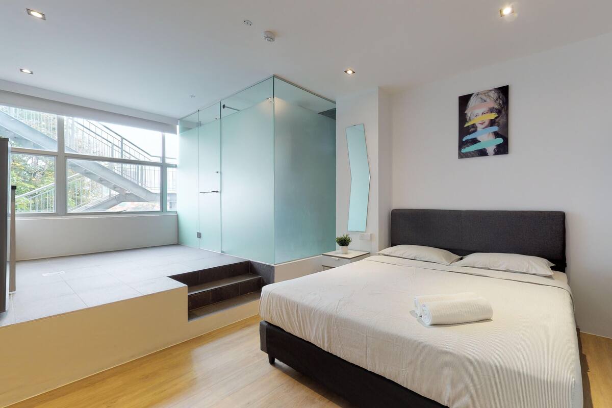 Camera da letto moderna con un letto grande, doccia a vetro e vista su una scala che conduce a una zona esterna.