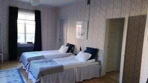 Un dormitorio con dos camas, un radiador, una ventana con cortinas y una alfombra estampada.