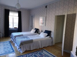 A bedroom with two beds, a radiator, a window with curtains, and a patterned carpet.