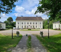 A large, symmetrical building with a central entrance, surrounded by a gravel driveway and grassy areas.